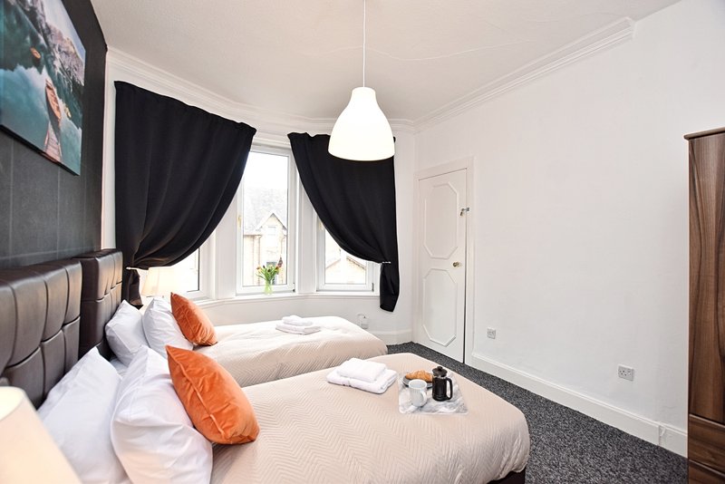 Bright bedroom with two single beds, orange pillows, black curtains and pendant light