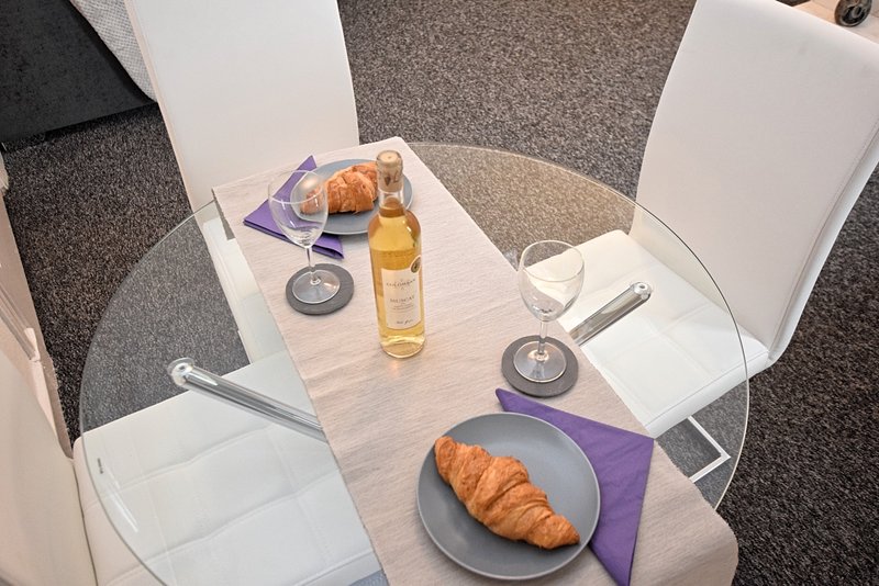 Dining table set for two with croissants, oil bottle, glasses and purple napkins