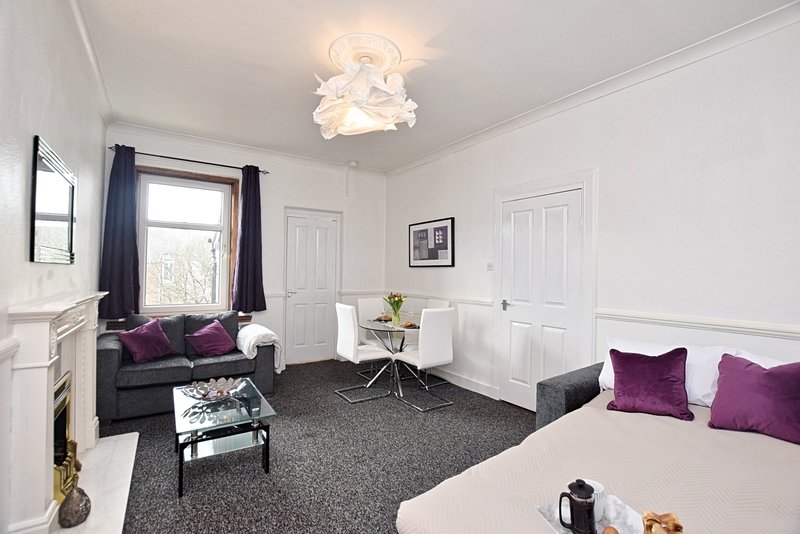 Bright bedroom with double bed, seating area, dark sofa and modern ceiling light