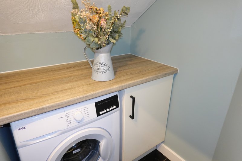 Laundry room with white washing machine, wooden countertop, and dried flowers in vase