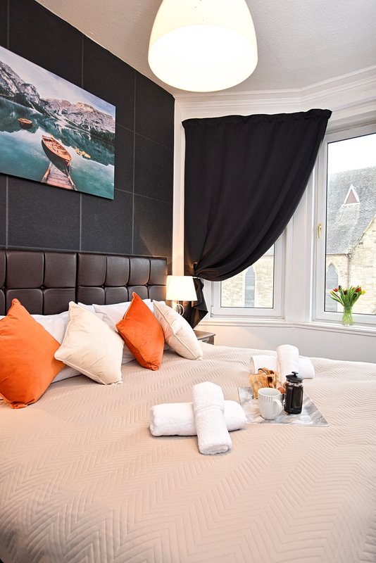 Modern bedroom with double bed, orange cushions, black headboard and pendant light fixture