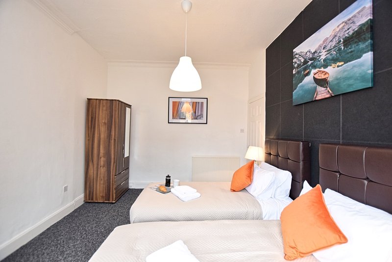 Modern bedroom with two single beds, orange cushions, pendant lighting and wall-mounted TV