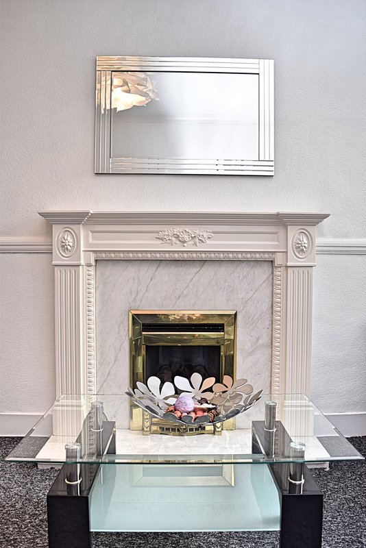 Fireplace with white marble surround, brass insert with lit coals, and mirror above