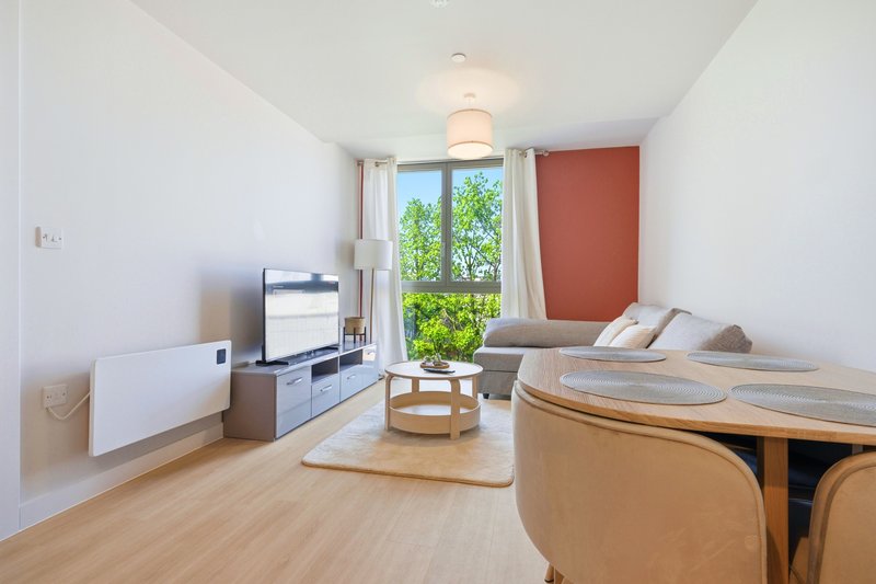 Modern studio apartment with bed, TV, desk, wooden flooring and large window overlooking greenery