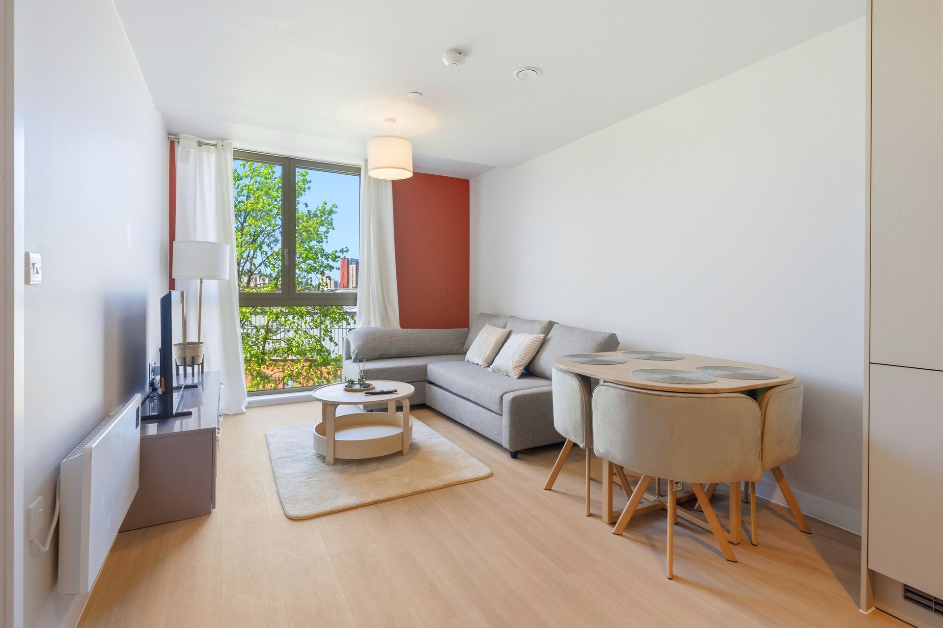 Modern living room with gray sofa, wooden dining table, and large window with garden view