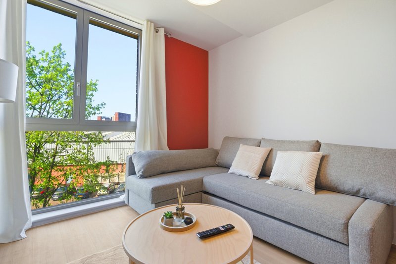 Modern living room with gray corner sofa, round wooden table, and balcony view of greenery
