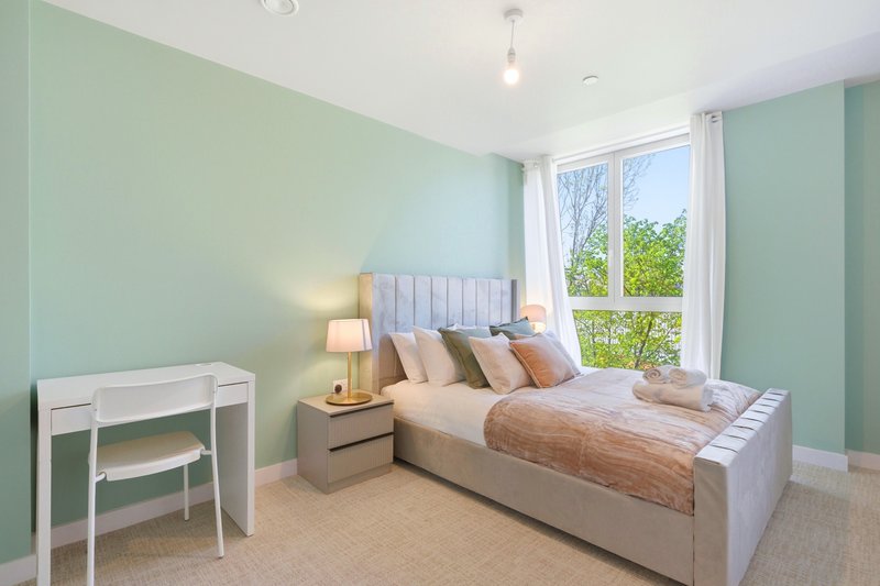 Bright bedroom with mint-green walls, double bed, desk, and window overlooking garden