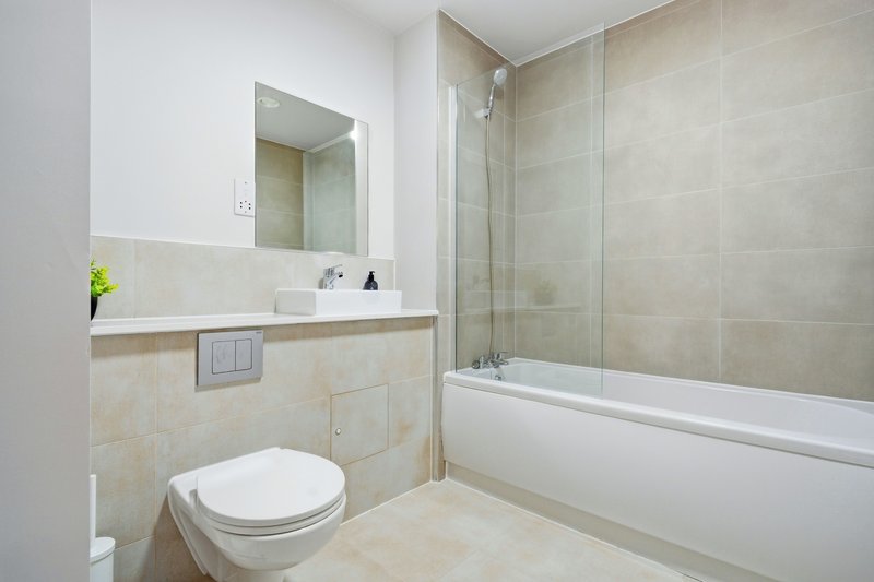Modern bathroom with toilet, vanity sink, mirror and bathtub with glass screen