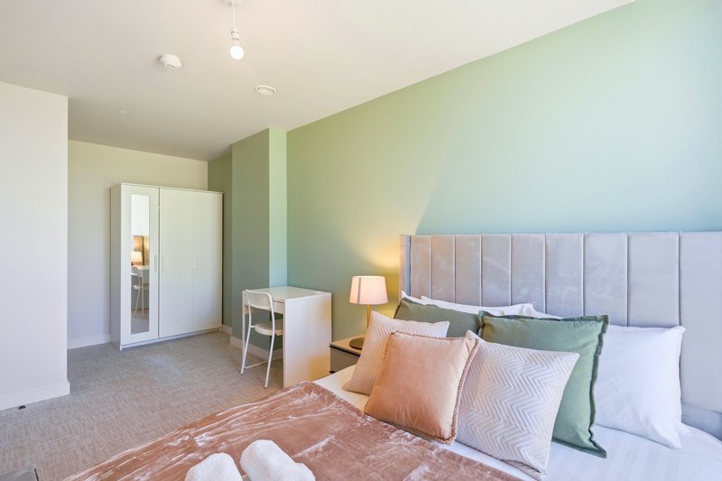 Modern bedroom with double bed, green accent wall, desk, and ensuite door