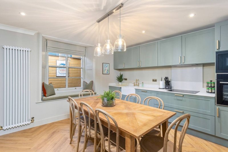 Modern kitchen-diner with wooden table, blue cabinetry, pendant lights and window seat