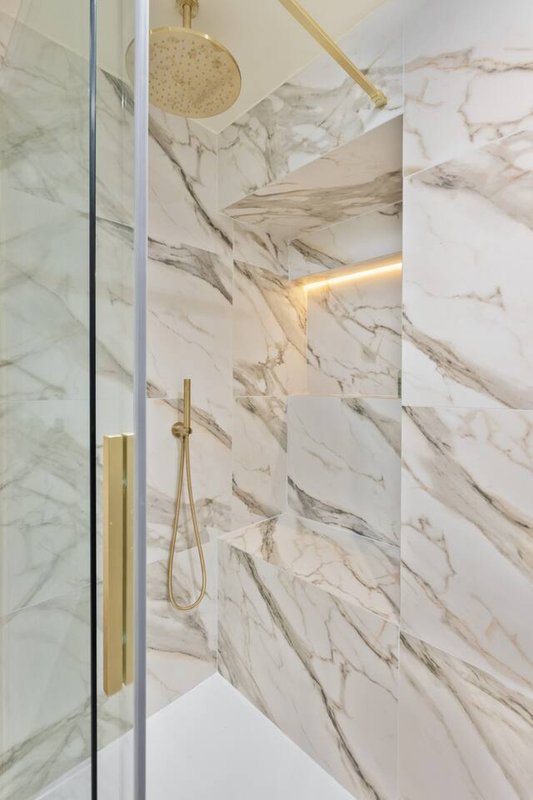 Modern bathroom shower enclosure with marble tiles, brass fixtures and recessed lighting