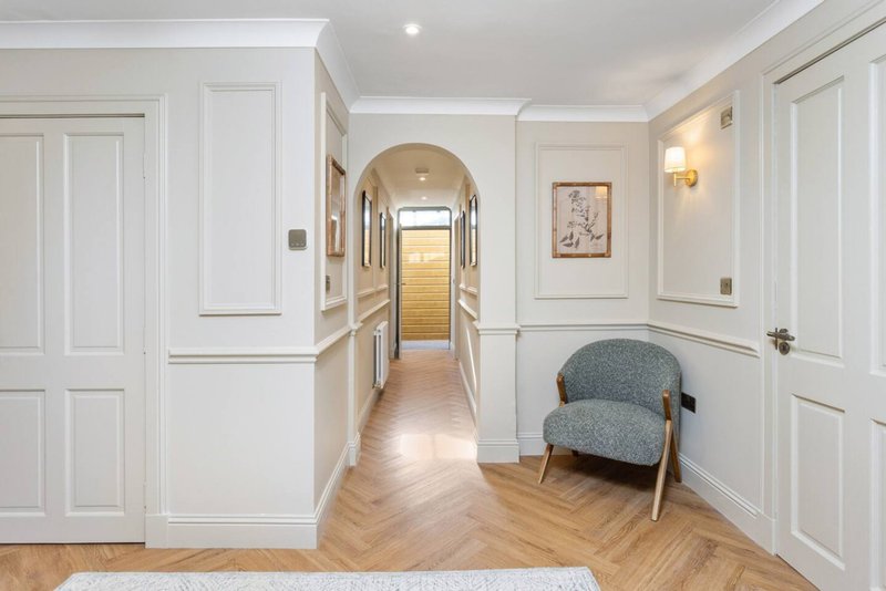 Bright hallway with white panelled doors, wooden flooring, grey armchair and framed artwork on wall