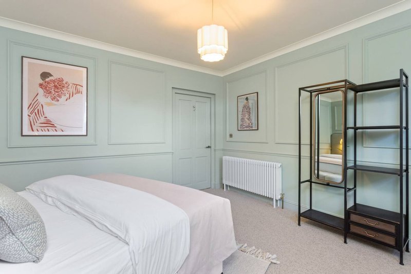 Pale blue bedroom with double bed, white bedding, framed artwork, and black metal shelving unit