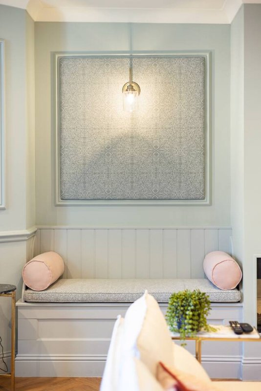 Built-in window seat with pink cushions, white paneling, pendant light and potted plant