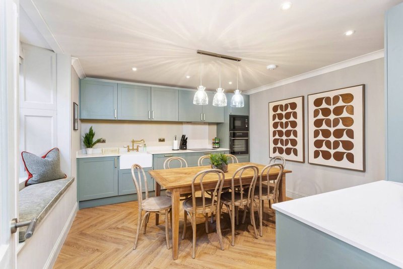 Modern open-plan kitchen and dining area with light blue cabinetry, wooden table, and framed wall art