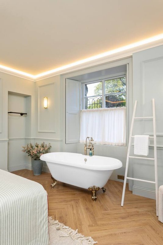 Bright bathroom with freestanding white bathtub, wooden floor, window with white curtains