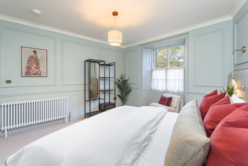Bright bedroom with double bed, panelled walls, window, radiator and modern furnishings