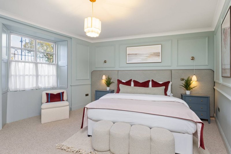 Bright bedroom with double bed, burgundy pillows, pale bedding, upholstered ottoman, and mint-green panelled walls