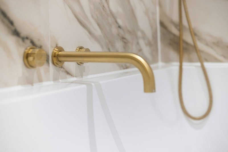 Modern bathroom with gold wall-mounted faucet and white bathtub edge