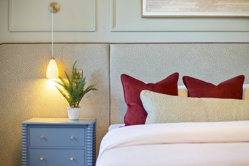 Modern bedroom with bed, burgundy cushions, blue nightstand, potted plant and pendant lamp