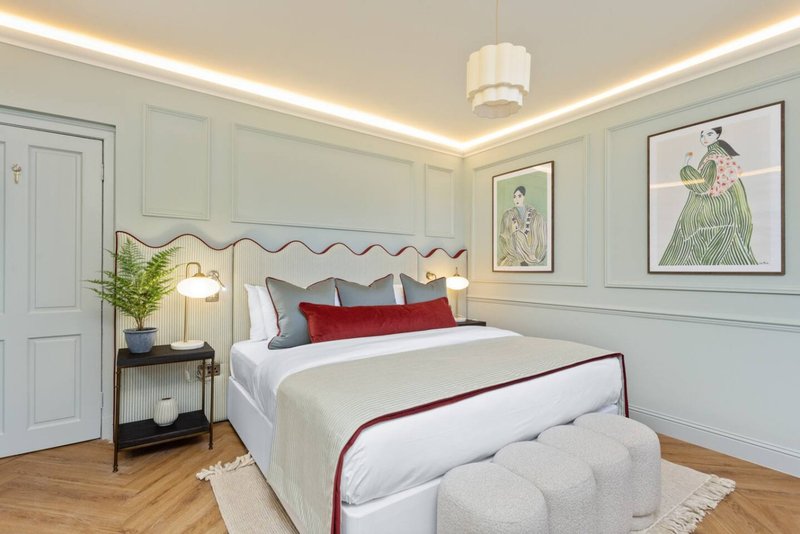 Elegant bedroom with upholstered headboard, white bedding, red accents, and framed artwork