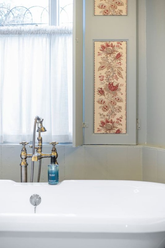 Modern bathroom with freestanding white bathtub, brass faucet, and floral wall art