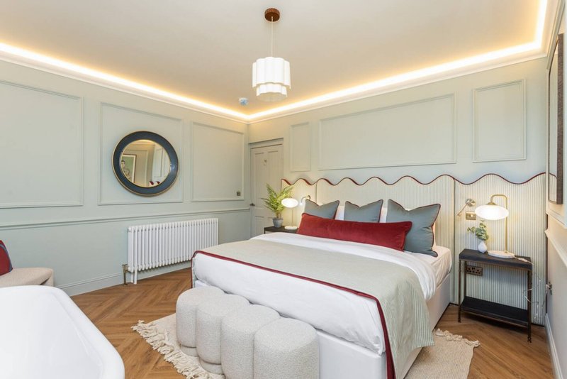 Bright modern bedroom with double bed, decorative pillows, round mirror, and ceiling lighting