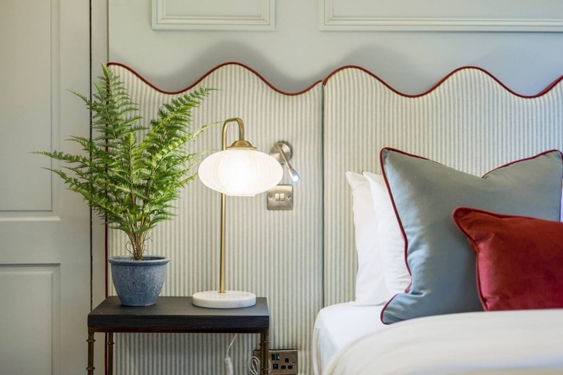 Bedroom bedside table with potted fern, pendant lamp, and pillows on bed