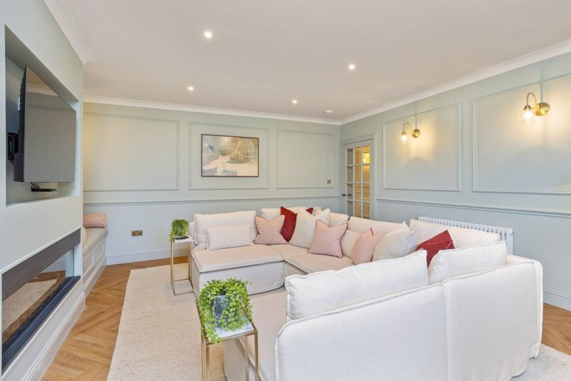 Modern living room with white sectional sofa, fireplace, wall-mounted TV, and pendant lighting