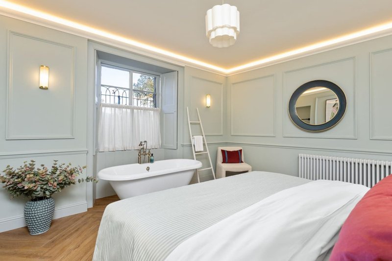 Bright modern bedroom with double bed, freestanding bathtub, round mirror and soft ambient lighting