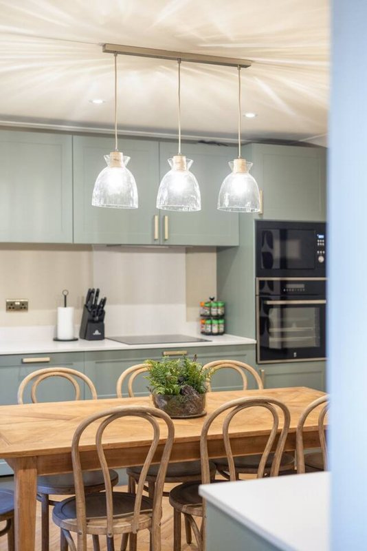Modern kitchen with sage green cabinetry, wooden dining table, pendant lights and built-in appliances