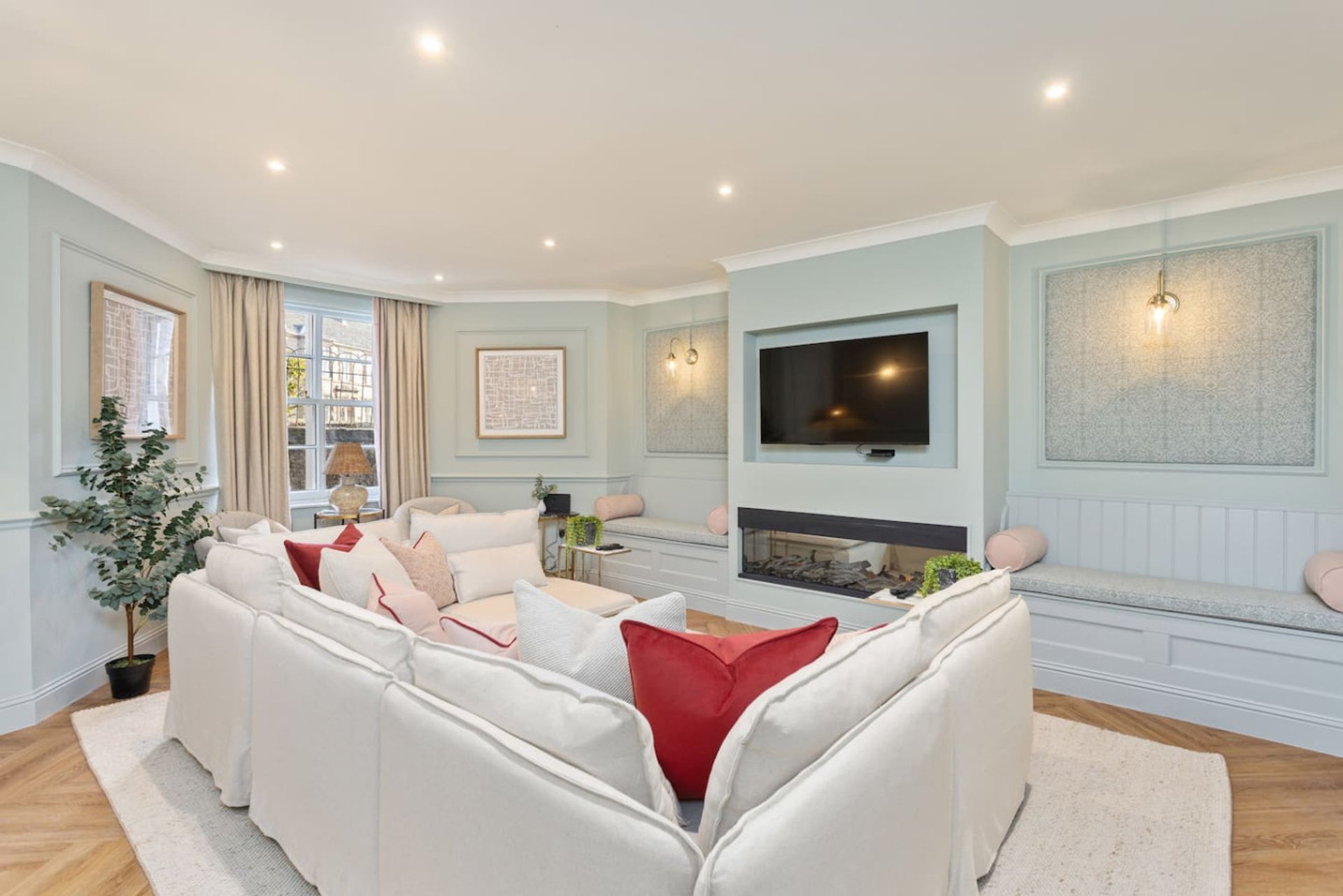 Modern living room with white corner sofa, fireplace, wall-mounted TV, and light blue panelling