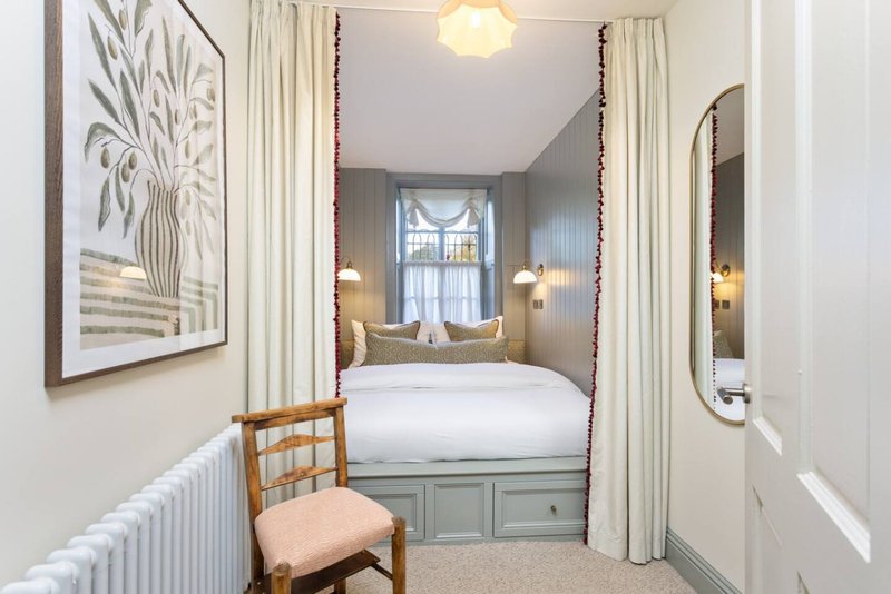 Bedroom with four-poster bed, cream curtains, wooden chair, framed botanical art and wall sconce lighting