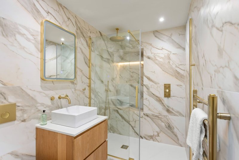Modern bathroom with marble walls, wooden vanity, vessel sink, and glass shower enclosure