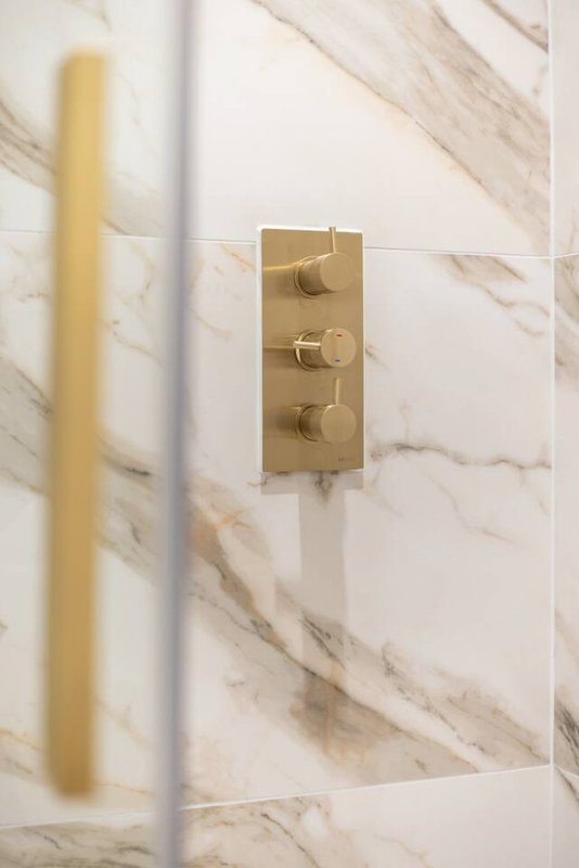 Bathroom wall with marble tiles and brass shower valve control