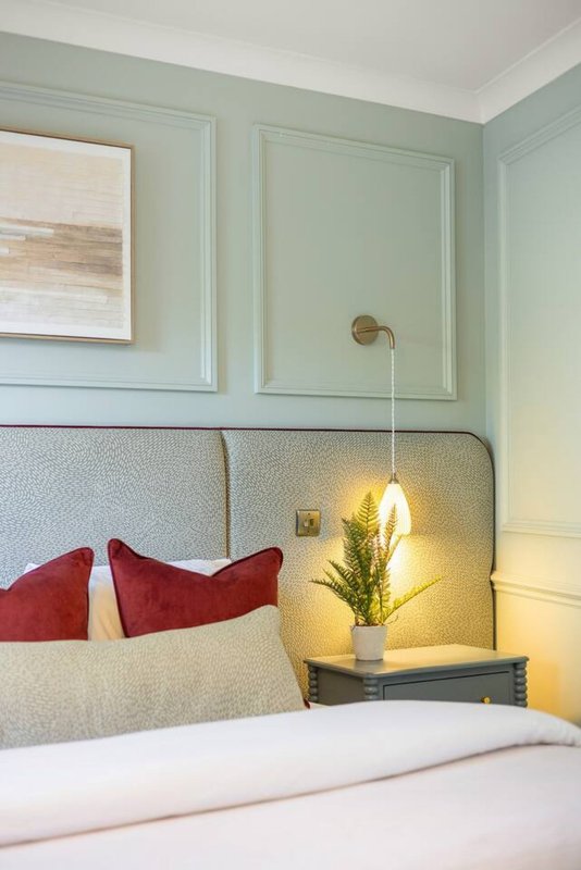 Bedroom with upholstered headboard, red cushions, pendant lamp and pale green panelled walls