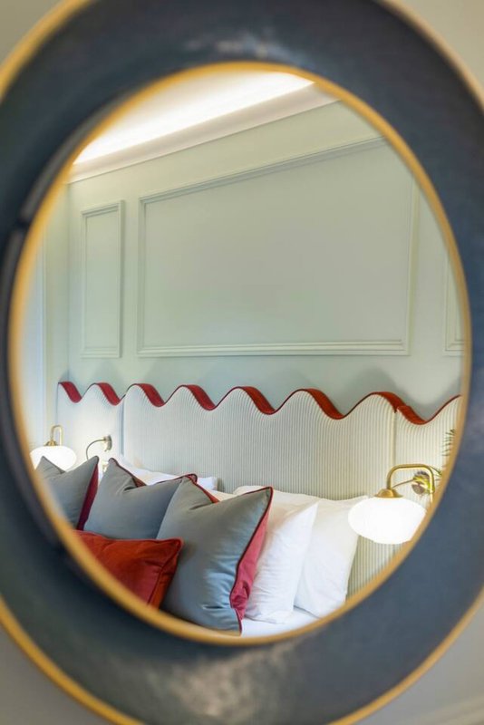 Bedroom with bed, decorative pillows and wavy headboard, viewed through oval mirror