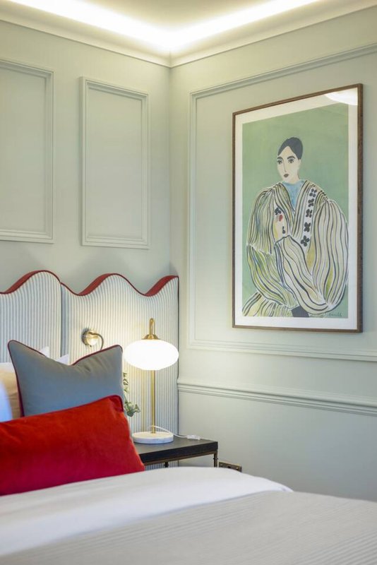 Bedroom with white panelled walls, framed portrait artwork, red cushion, and bedside lamp