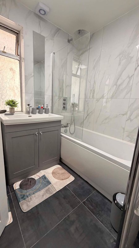 Modern bathroom with grey vanity, marble tile walls, shower enclosure and bathtub