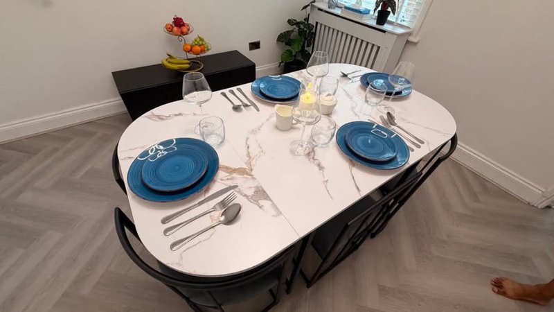 Dining table set for four with blue plates, glasses, and cutlery on white surface