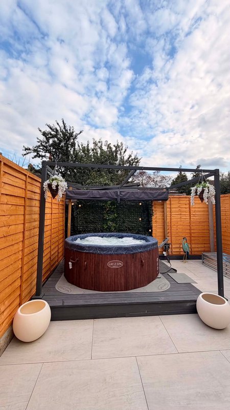 Outdoor patio with hot tub, wooden pergola, planters, and paved flooring