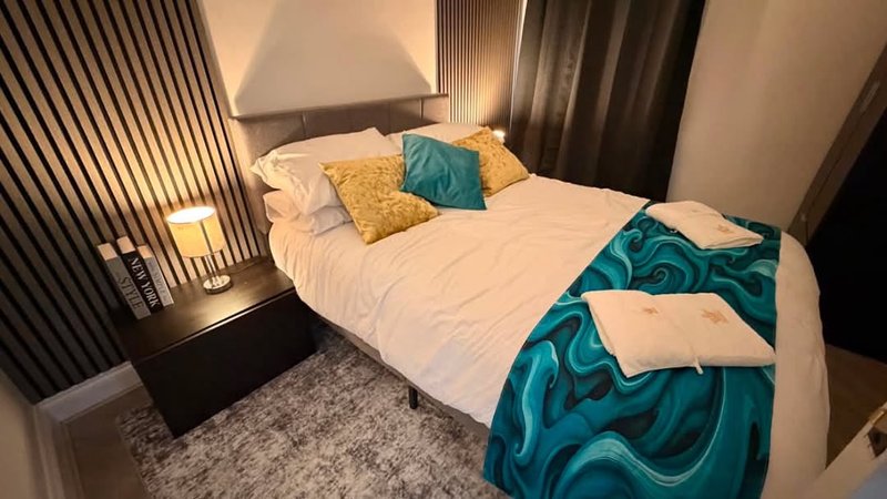 Modern bedroom with double bed, teal and yellow pillows, dark headboard and bedside lamp