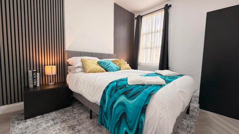 Modern bedroom with double bed, turquoise throw, decorative pillows and bedside lamp