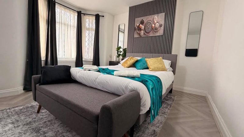 Modern bedroom with double bed, colorful cushions, bench seating, and large windows with curtains