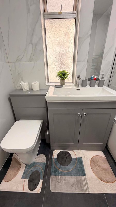 Modern bathroom with gray vanity, toilet, window, and coordinating bath mats