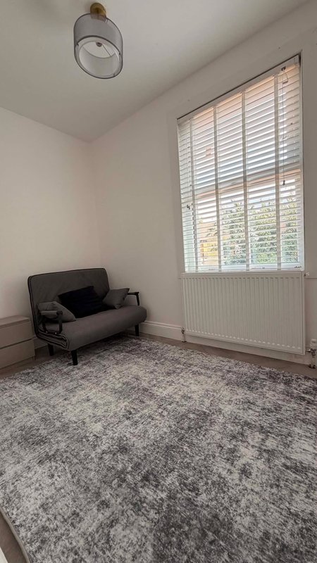 Bright bedroom with futon sofa, large window with shutters, pendant light, and gray carpet