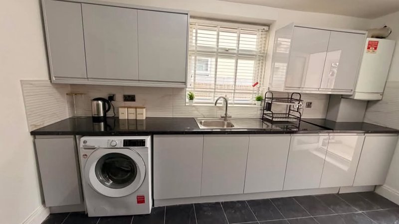 Modern kitchen with white cabinetry, black countertop, integrated washing machine and sink
