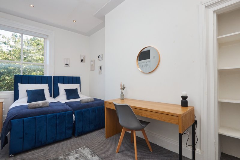 Modern bedroom with blue velvet bed, wooden desk, round mirror and built-in shelving