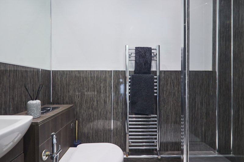 Modern bathroom with dark wood paneling, white sink, toilet, and heated towel rack