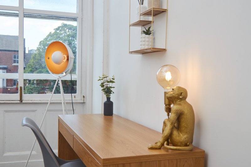 Modern workspace with wooden desk, desk lamp, gold cat figurine, and large window overlooking street